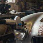 Bringing Classics Back to Life with Laser-Based Restoration Tools Mechanic using a handheld laser cleaning tool on a vintage classic car’s rusted fender inside an automotive restoration workshop.